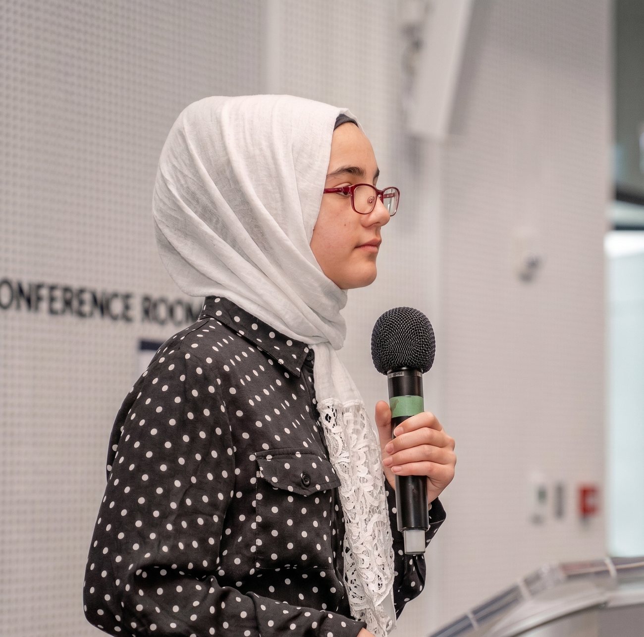 A young Muslim woman speaking confidently at a podium